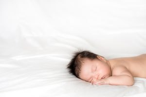Beba sa kosom spava na bijeloj, čistoj posteljini