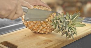 A woman cuts a pineapple on a wooden cutting board